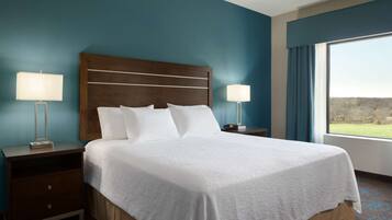 Una habitación de hotel con una cama grande, dos mesitas de noche con lámparas, vistas al exterior a través de una ventana y una pared azul.