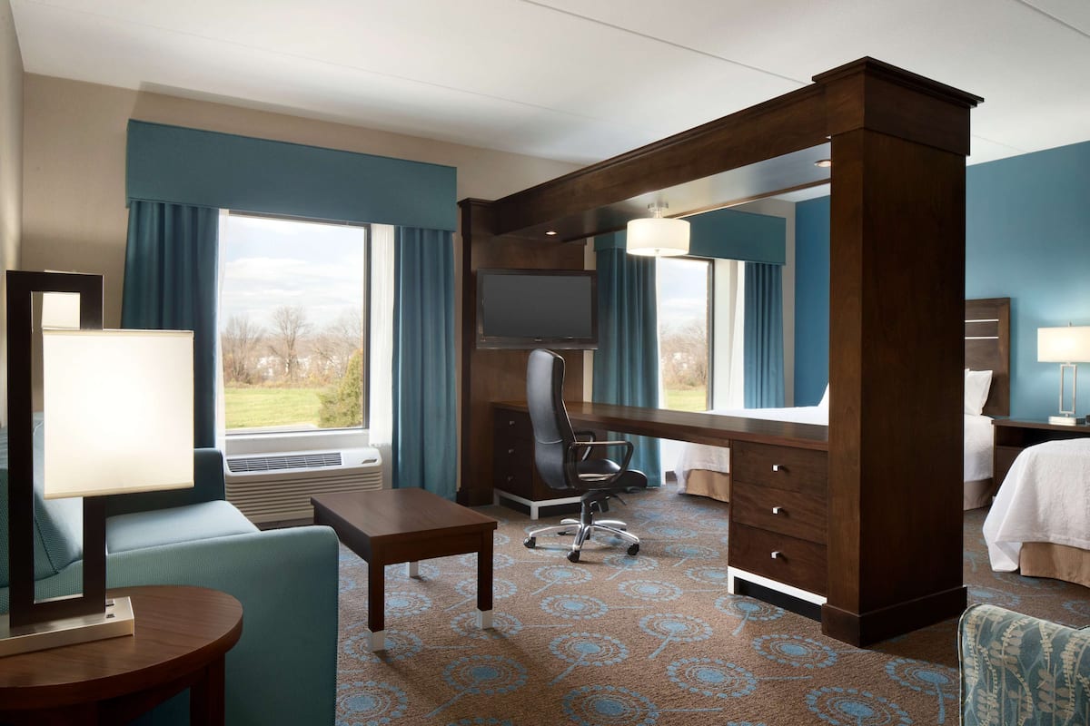 A hotel room with a large desk, a chair, a bed, a TV, and a view of the outdoors.