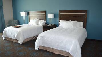 A hotel room with two beds, a nightstand with lamps, a chair, and a patterned carpet.