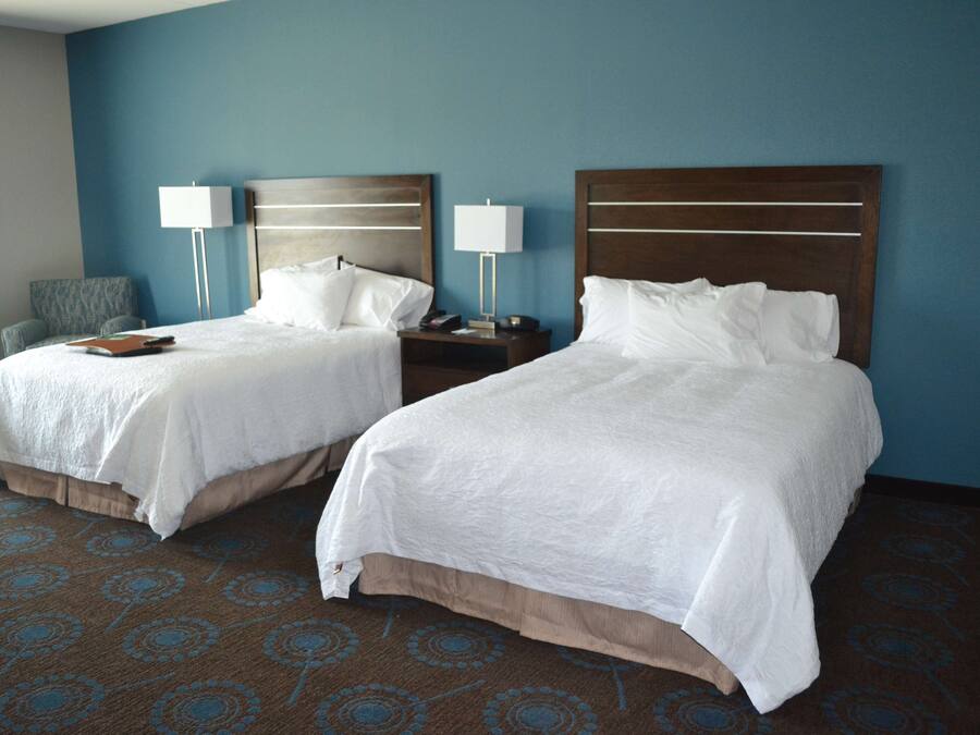 A hotel room with two beds, a nightstand with lamps, a chair, and a patterned carpet.
