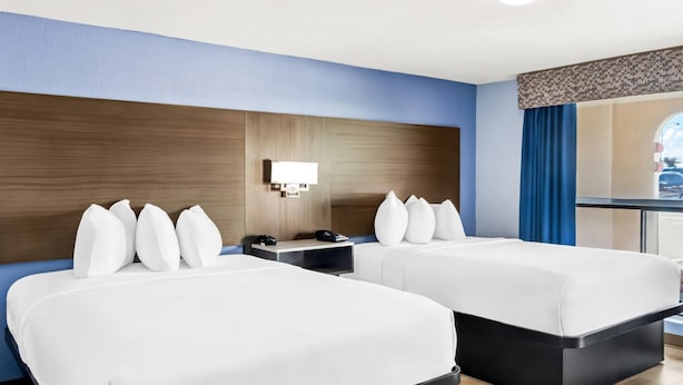 Habitación de hotel con dos camas, una mesita de noche con teléfono, una lámpara de pared y una ventana con cortinas azules.