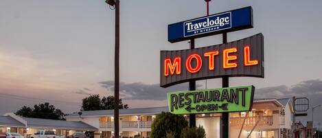 Un motel con un letrero de neón que indica que es un Travelodge by Wyndham, un restaurante y un motel.