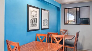 Un comedor con pared azul, cuadros enmarcados y una ventana con aire acondicionado.