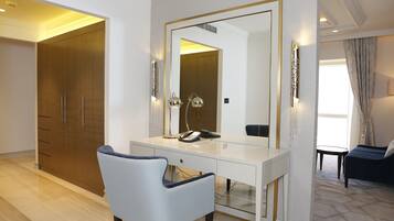 A hotel room with a white desk, a chair, a large mirror, a wardrobe, and a sofa.
