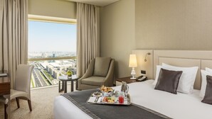 Une chambre d’hôtel avec un lit, une chaise, une petite table, un plateau avec des articles pour le petit-déjeuner, une lampe et un téléphone.