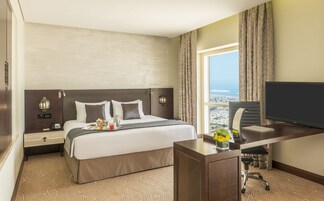 Habitación de hotel con cama, escritorio con televisor, silla, lámpara de escritorio y vista a la ciudad.