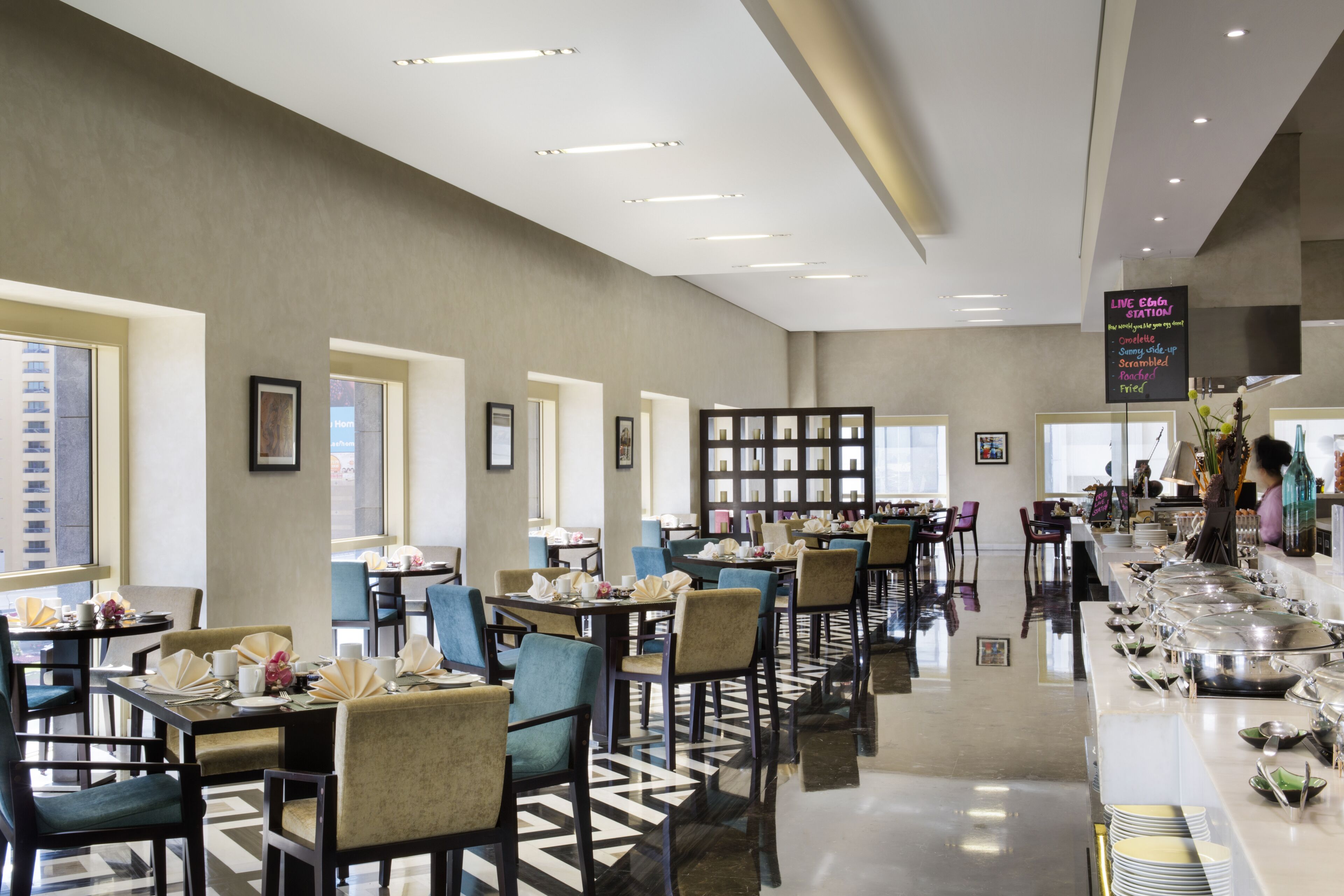 A modern hotel dining area with multiple tables and chairs, a buffet line, and a sign indicating a live station.