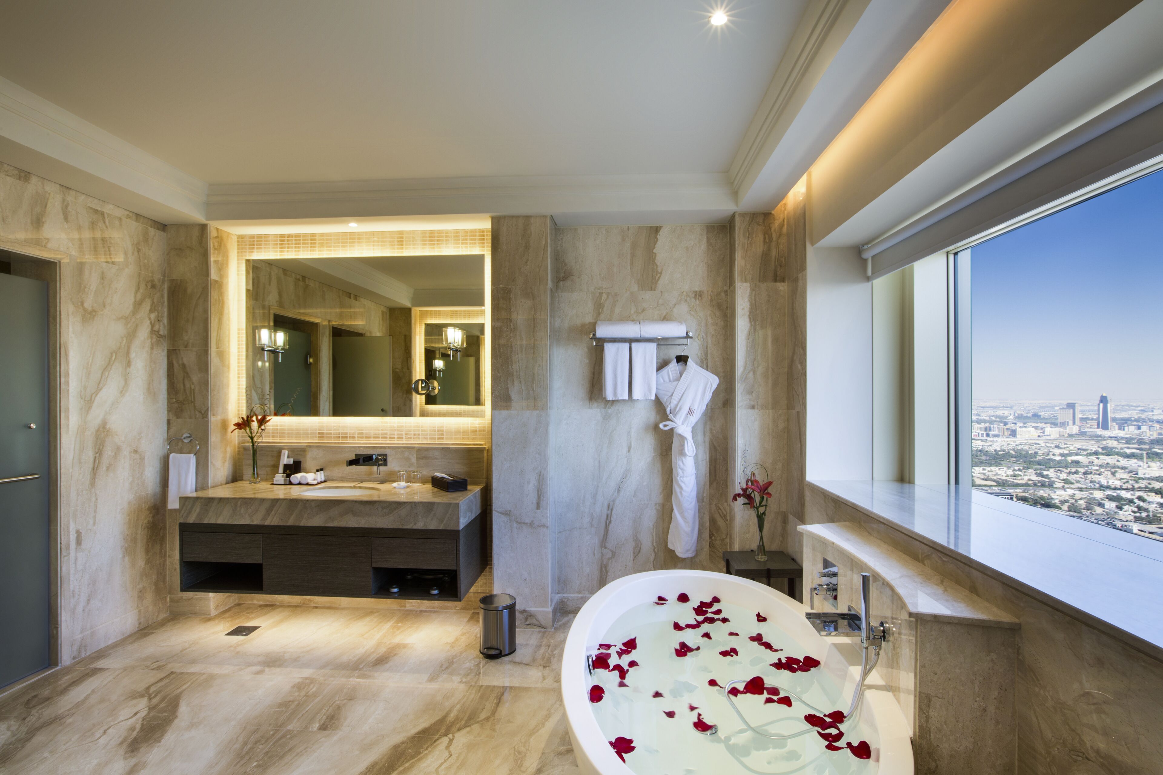 Un baño moderno con una bañera grande, un tocador con espejo y vistas a la ciudad a través de un ventanal.