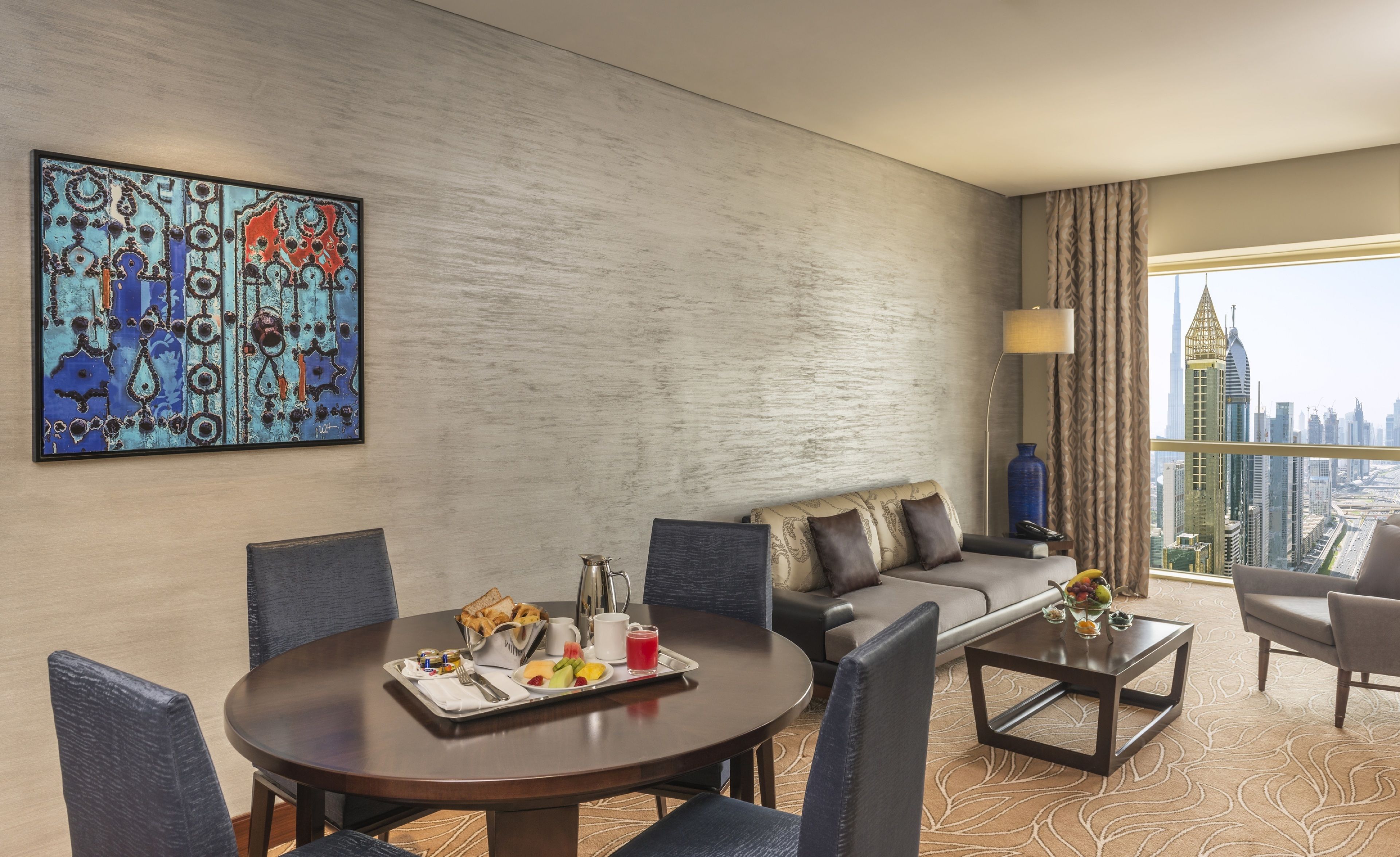 Une chambre d’hôtel avec une table à manger dressée pour le petit-déjeuner, un canapé et une vue sur la ville.
