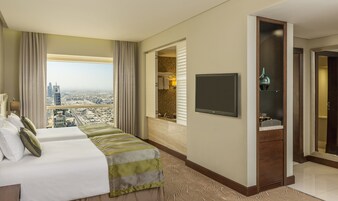 A hotel room with a large bed, a television, a bathroom with a mirror, and a view of the cityscape.