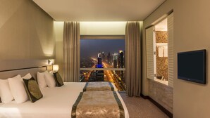 Une chambre d’hôtel avec un grand lit, une télévision, une fenêtre donnant sur la ville et une salle de bain avec un mur carrelé.