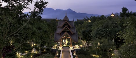 A traditional building with a central pathway leading to it, surrounded by greenery and trees.