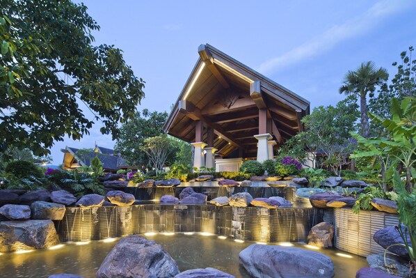 A modern building with a unique roof structure, surrounded by a landscaped garden with rocks and water features. - Anantara Xishuangbanna Resort (Xishuangbanna Dai)