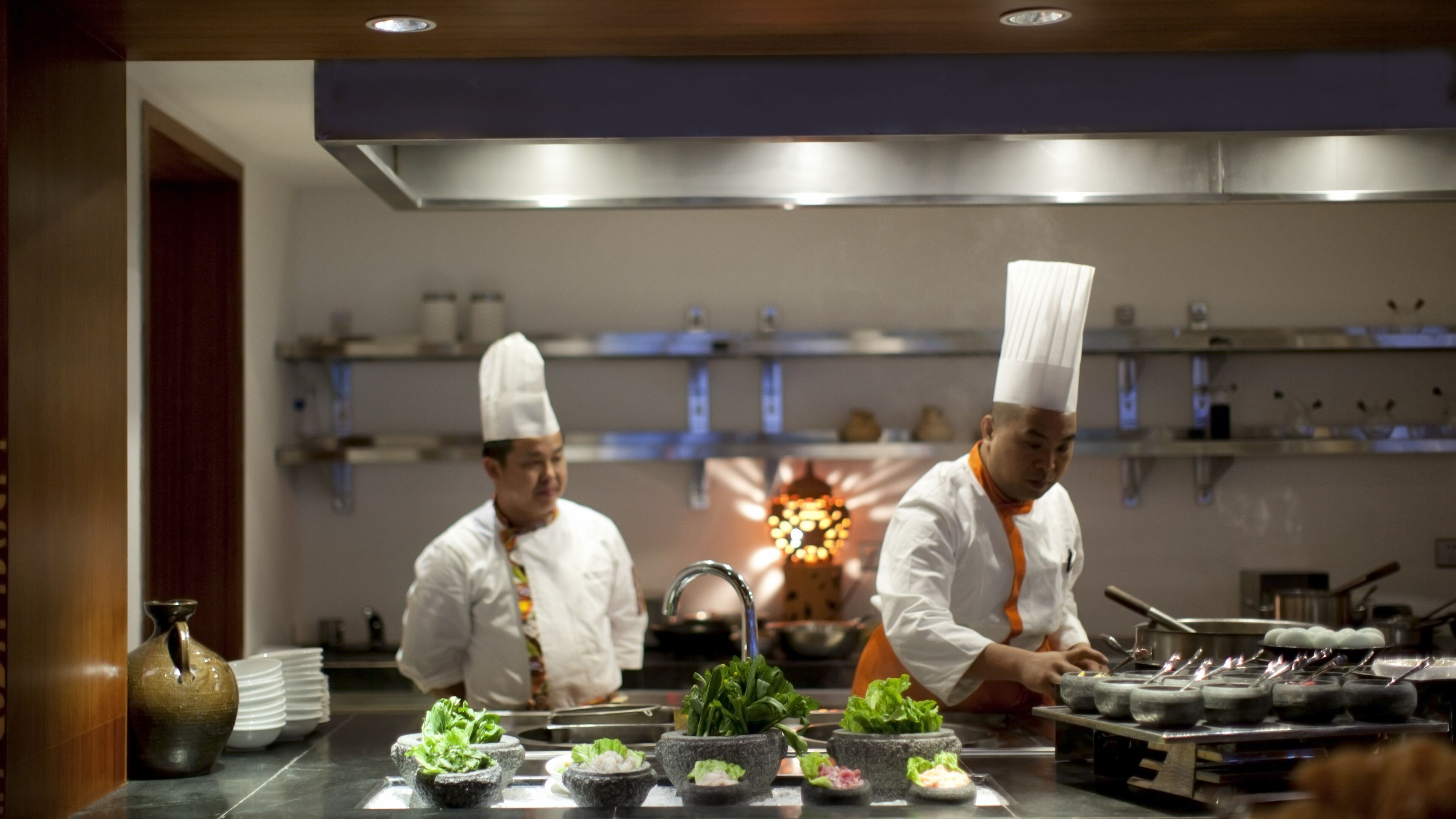 A professional kitchen with chefs preparing food, stainless steel appliances, and a modern interior design.