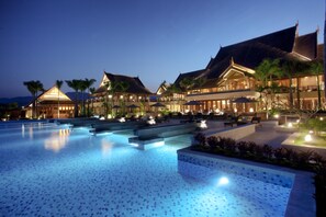 Un resort con una piscina grande, varias zonas de descanso y arquitectura tradicional.