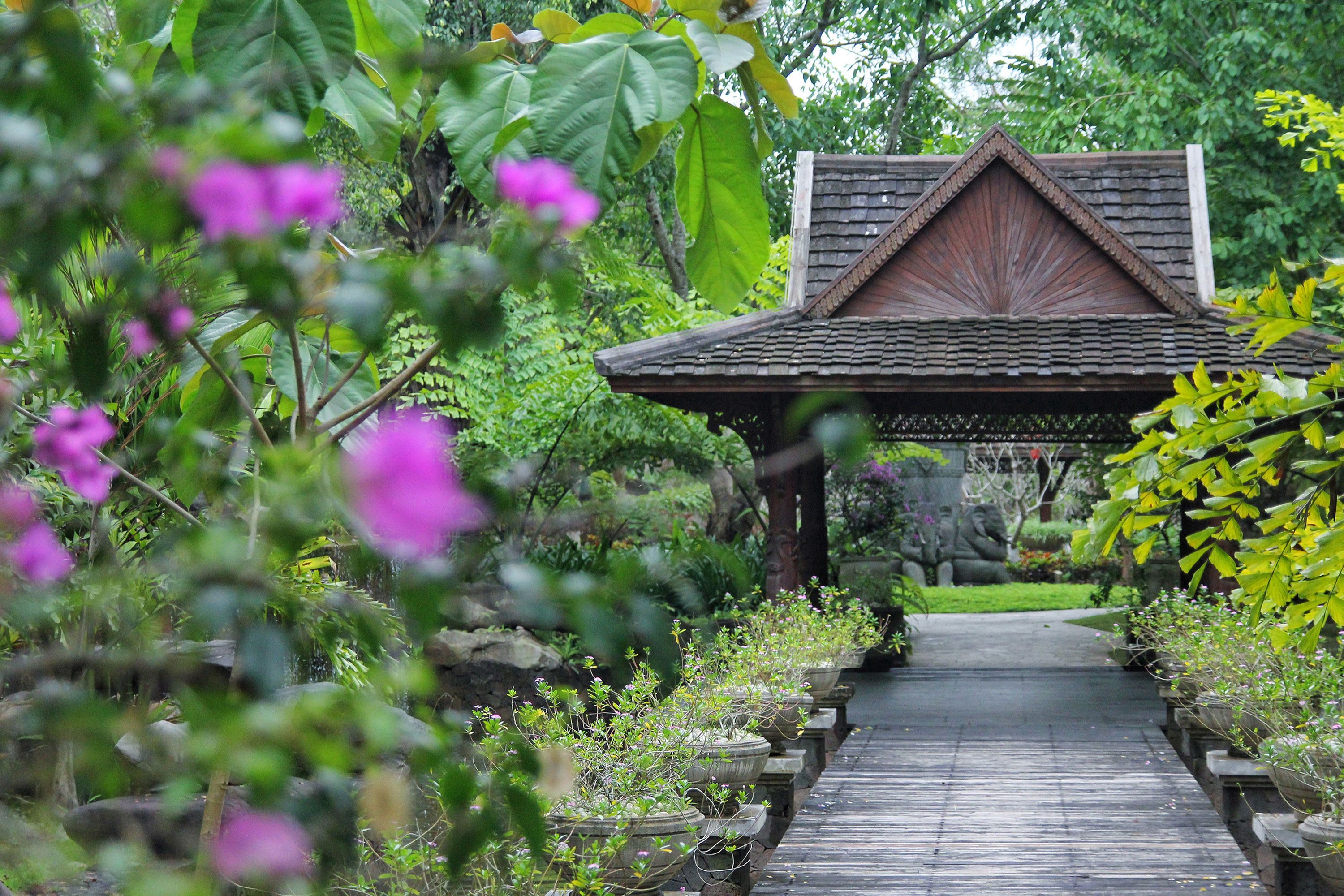 A traditional wooden pavilion with a tiled roof, surrounded by lush greenery and flowering plants.