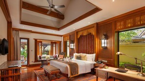 A spacious bedroom with a large bed, wooden furniture, a desk, and a view of the outdoors. - Anantara Xishuangbanna Resort (Xishuangbanna Dai)