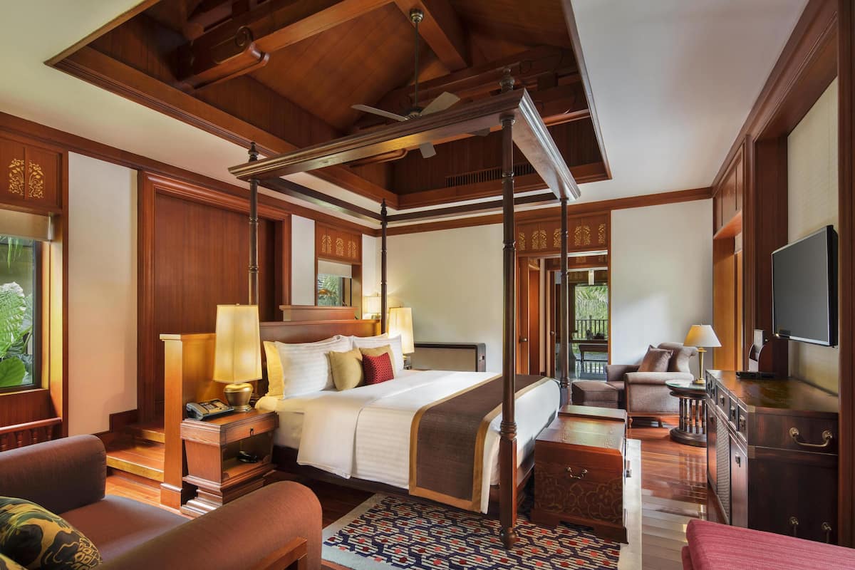 A spacious hotel room with a large bed, a sitting area with a sofa and armchairs, a television, and a wooden ceiling.