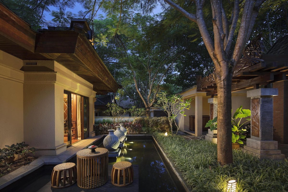 A serene outdoor area with a small water feature, seating, and lush greenery.