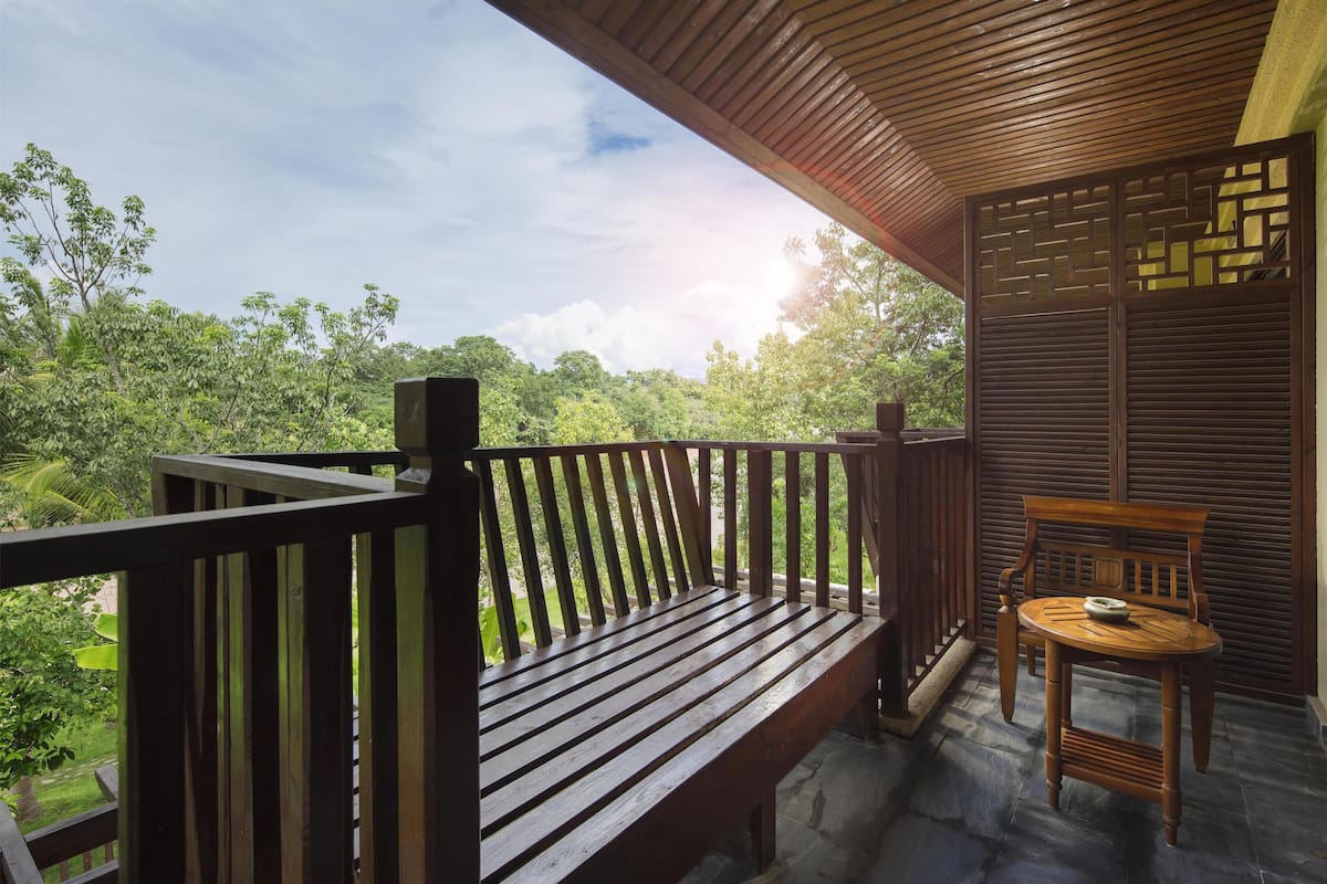 A wooden bench and table on a balcony with a view of lush greenery and trees.