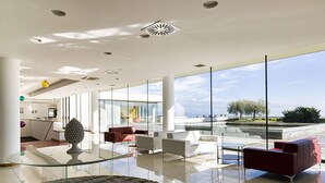 Een ruime lobby met een glazen bijzettafeltje, rode en witte banken en uitzicht op zee.