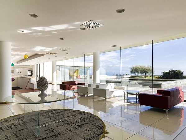 A spacious lobby with a glass coffee table, red and white sofas, and a view of the sea. - Esperia Palace Hotel (Zafferana Etnea)