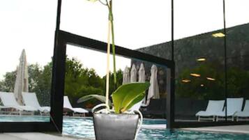 A modern indoor pool area with a large window, lounge chairs, and a potted orchid.