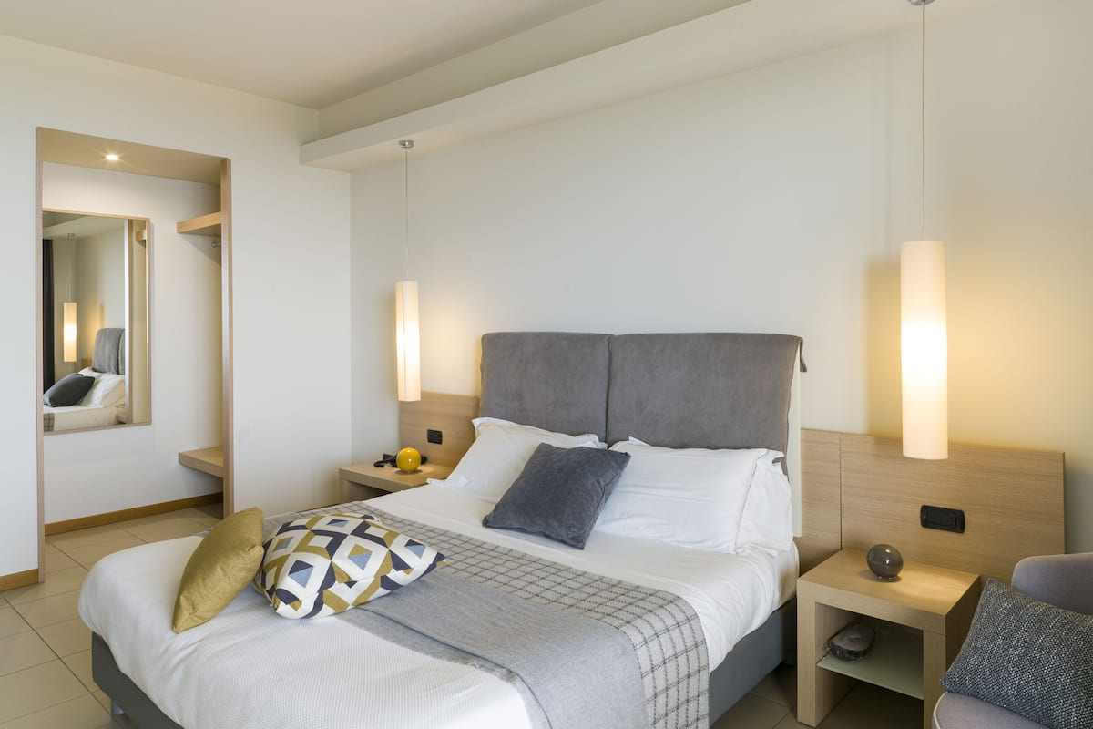 Una habitación de hotel moderna con una cama grande, mesitas de noche, un espejo y una lámpara colgante.