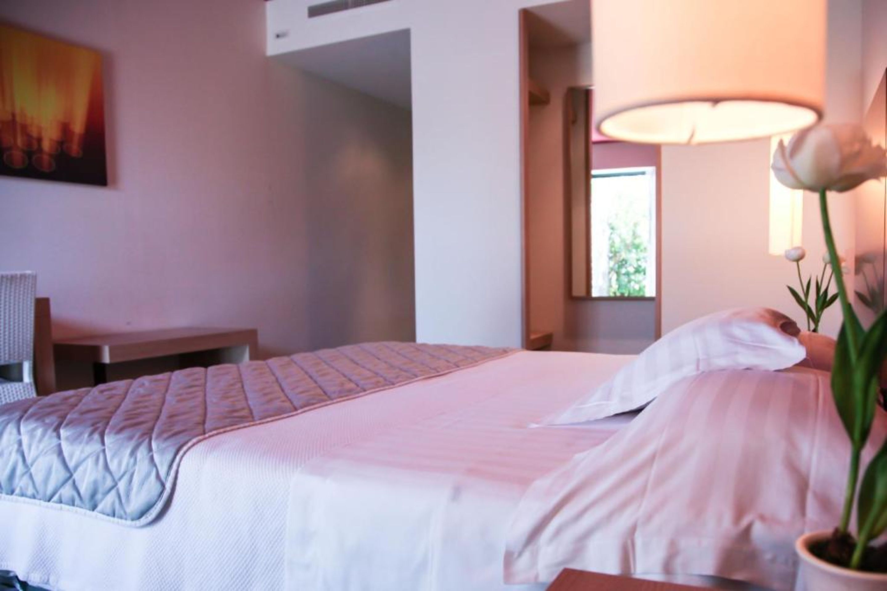 A hotel room with a bed, a desk, a lamp, and a potted plant.