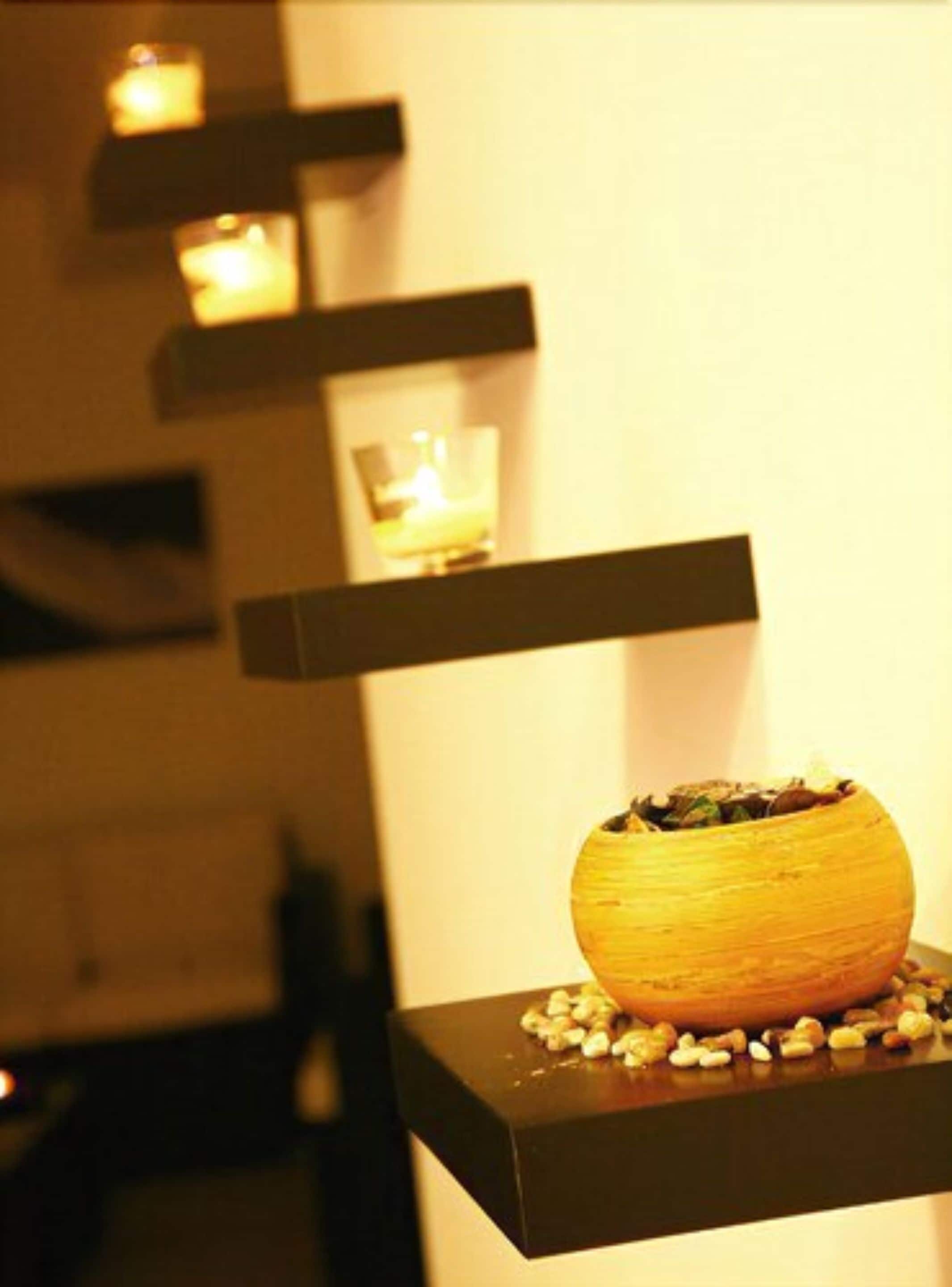A modern interior with a decorative bowl on a black shelf, surrounded by small objects, and lit candles on shelves.