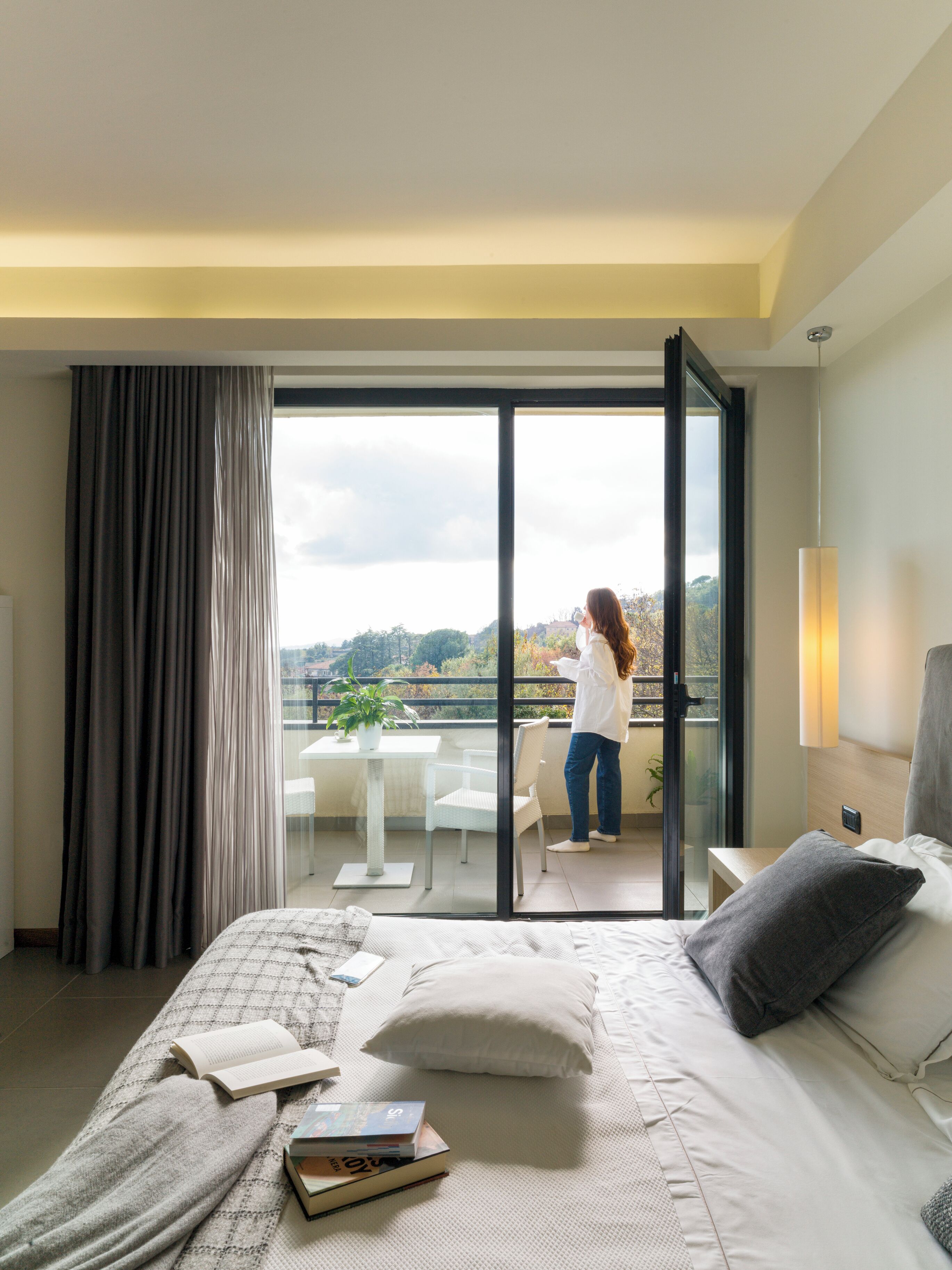 A bedroom with a bed, a balcony, a table with a plant, and a view of the outside.
