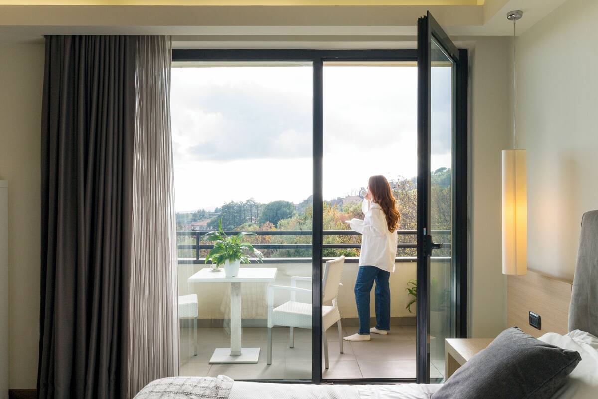 Un dormitorio con cama, balcón, una mesa con planta y vistas al exterior.