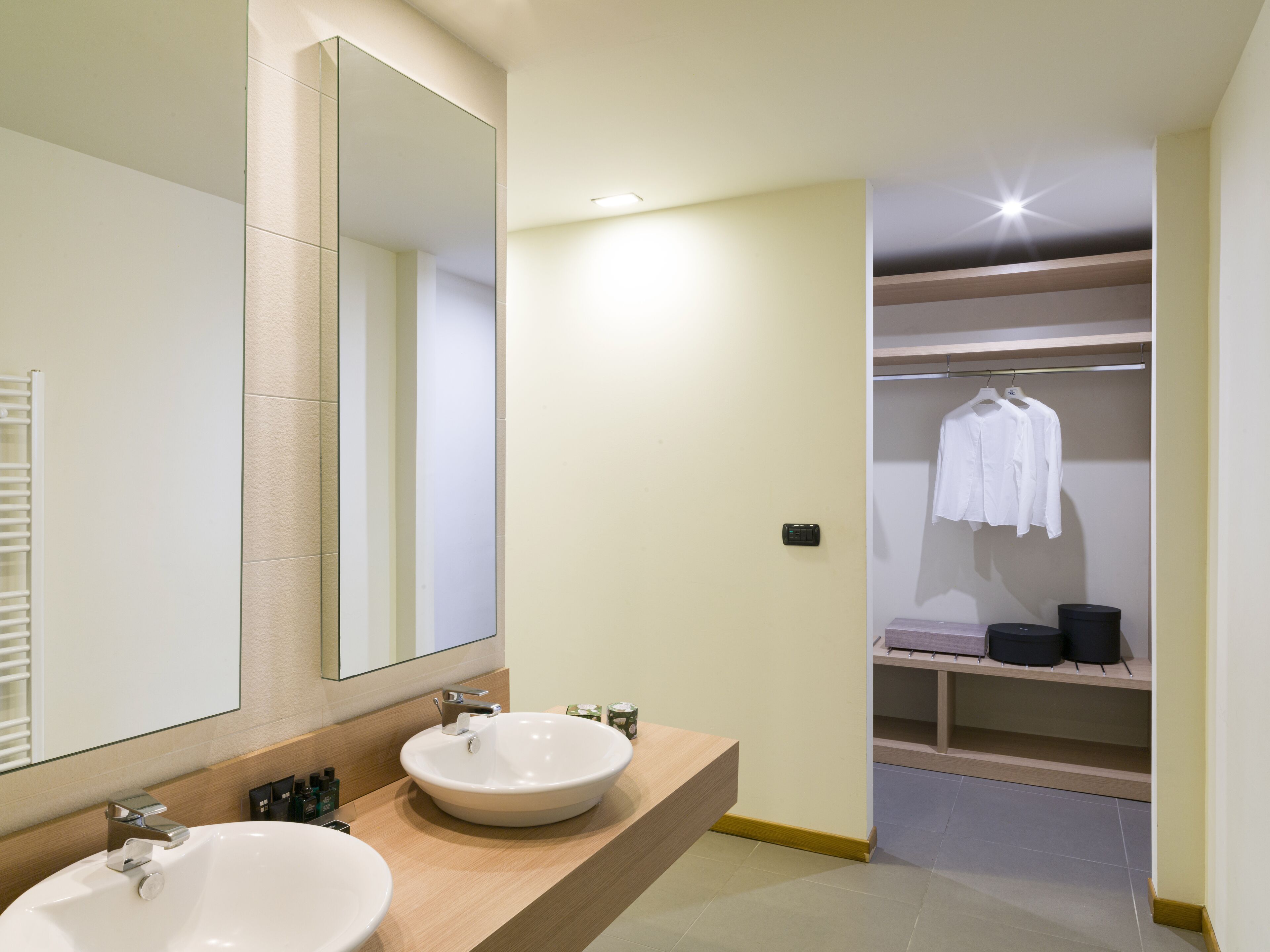 Un bagno moderno con uno specchio grande, due lavabi e una cabina armadio con abiti appesi.