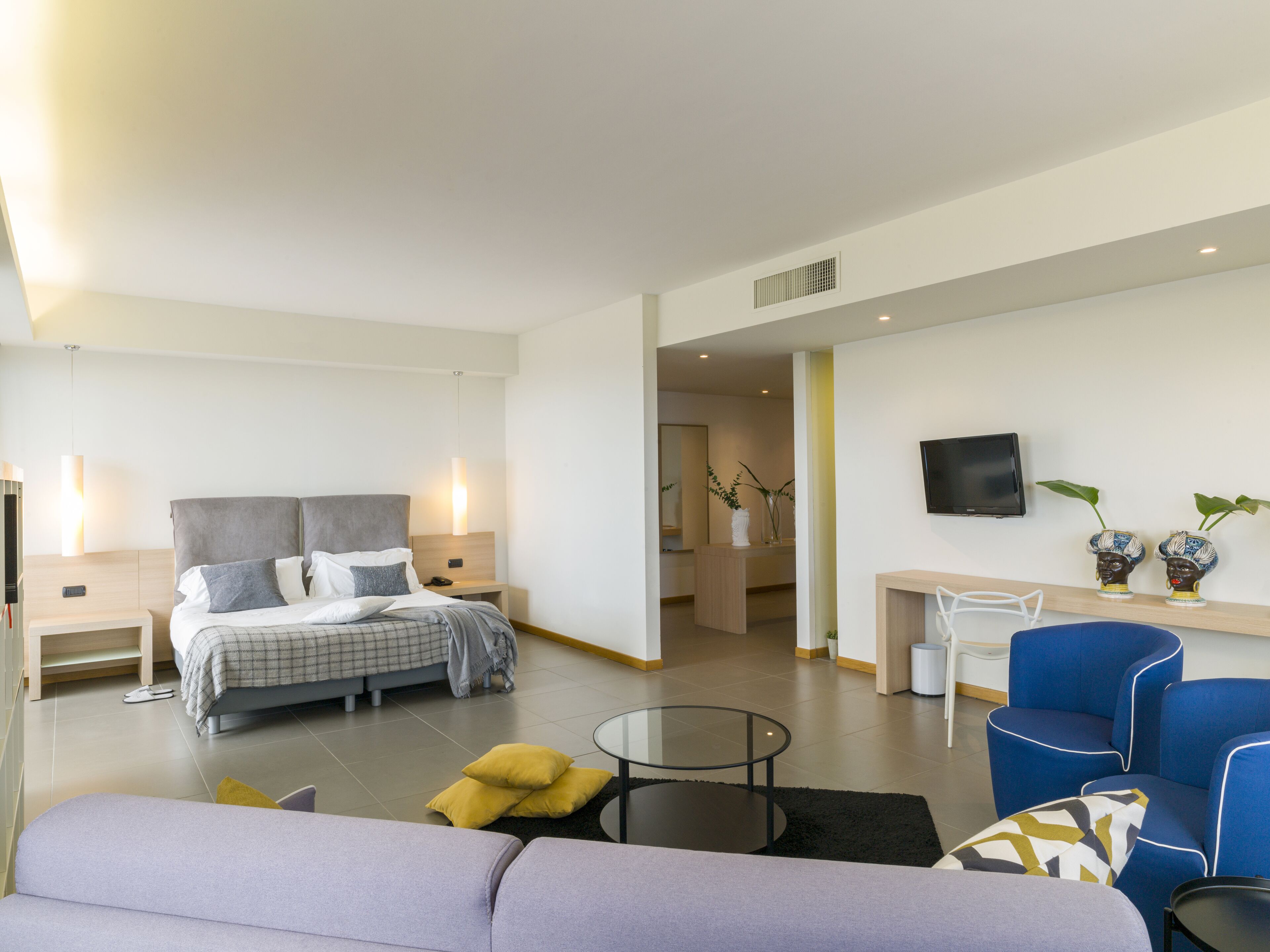 A modern hotel room with a bed, a sofa, a small table, and a TV.