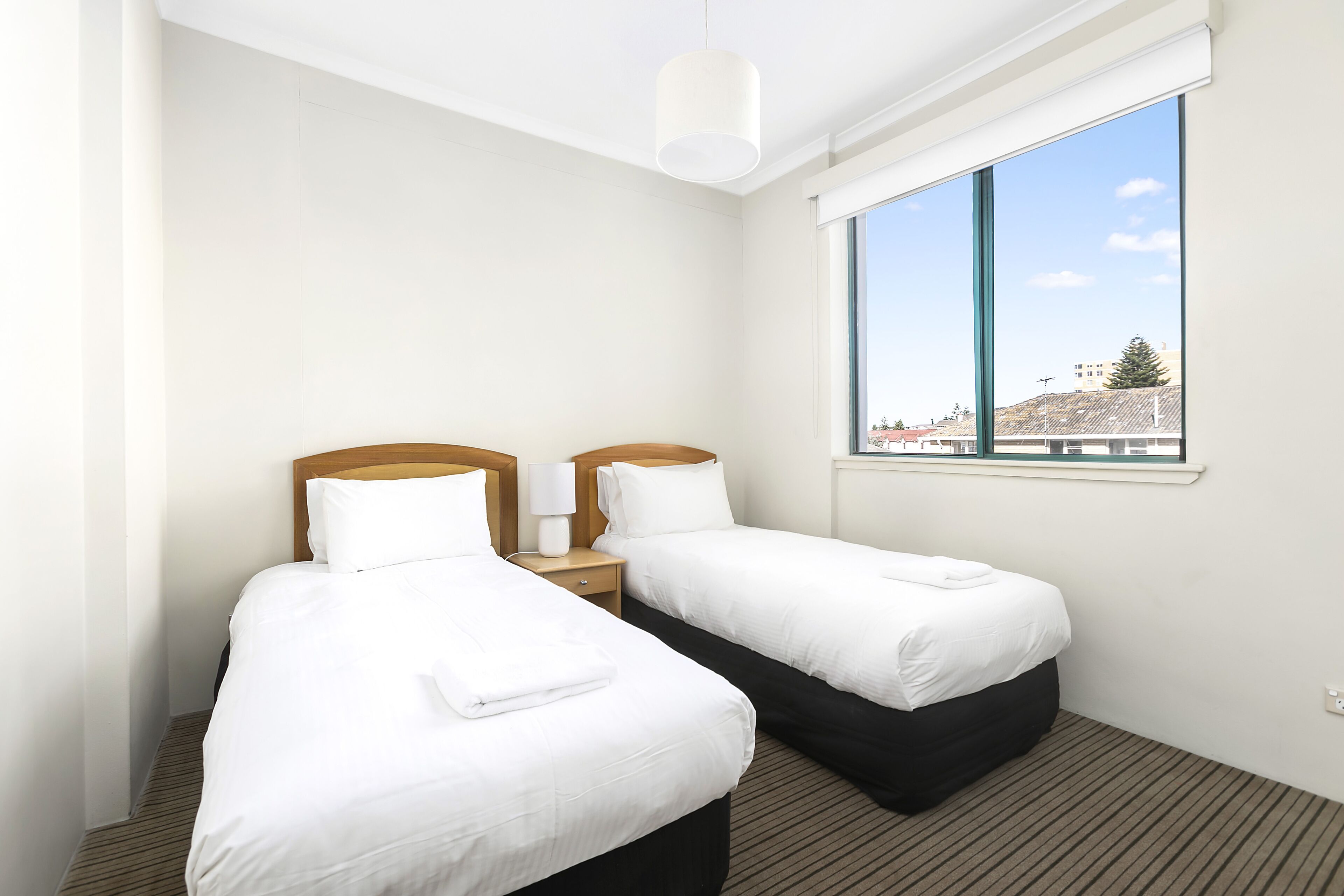 A hotel room with two single beds, a large window with a city view, and a modern ceiling light.
