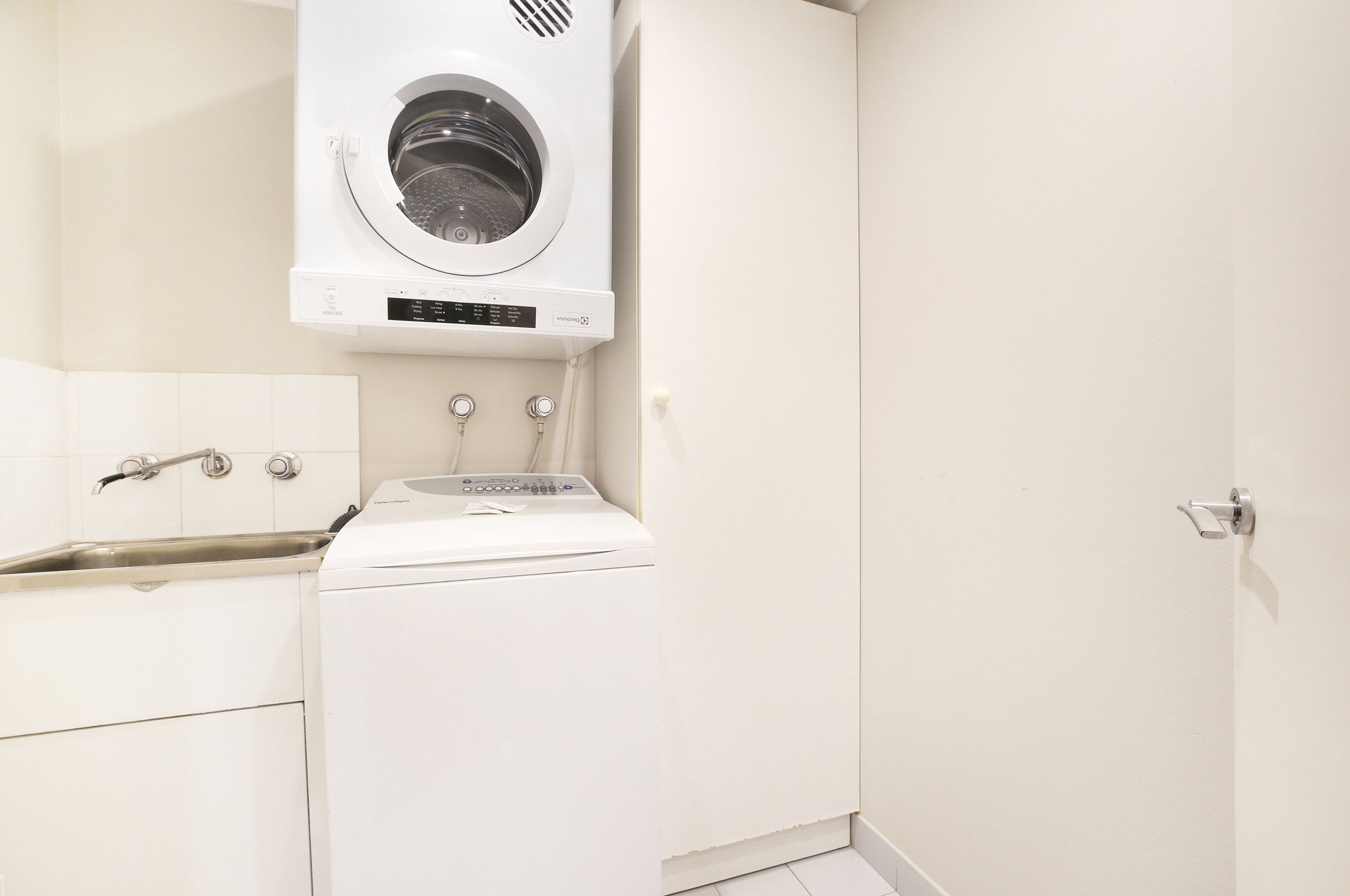 Een kleine wasruimte met een wasmachine, een wastafel en een kastje.