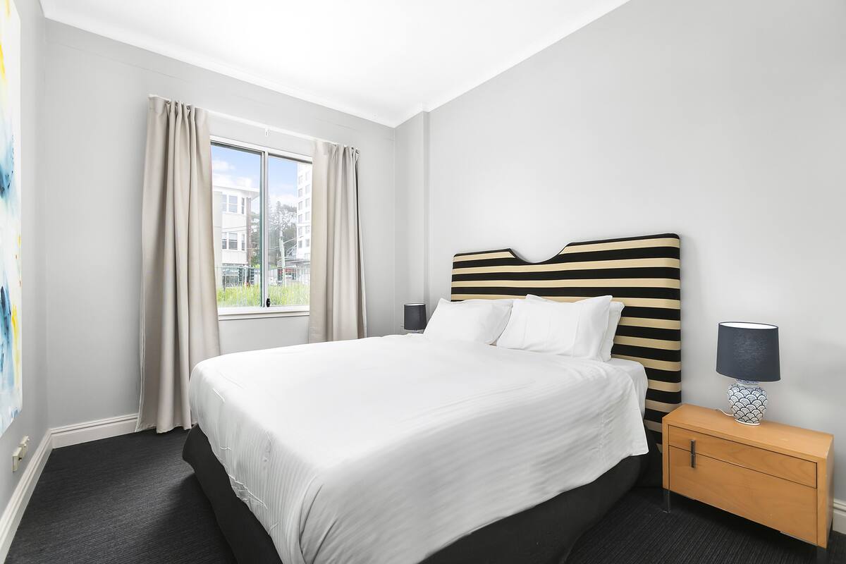 A neatly made bed with white linens, a striped headboard, and a bedside table with a lamp.