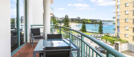 A balcony with a table and chairs, overlooking a beach and ocean.