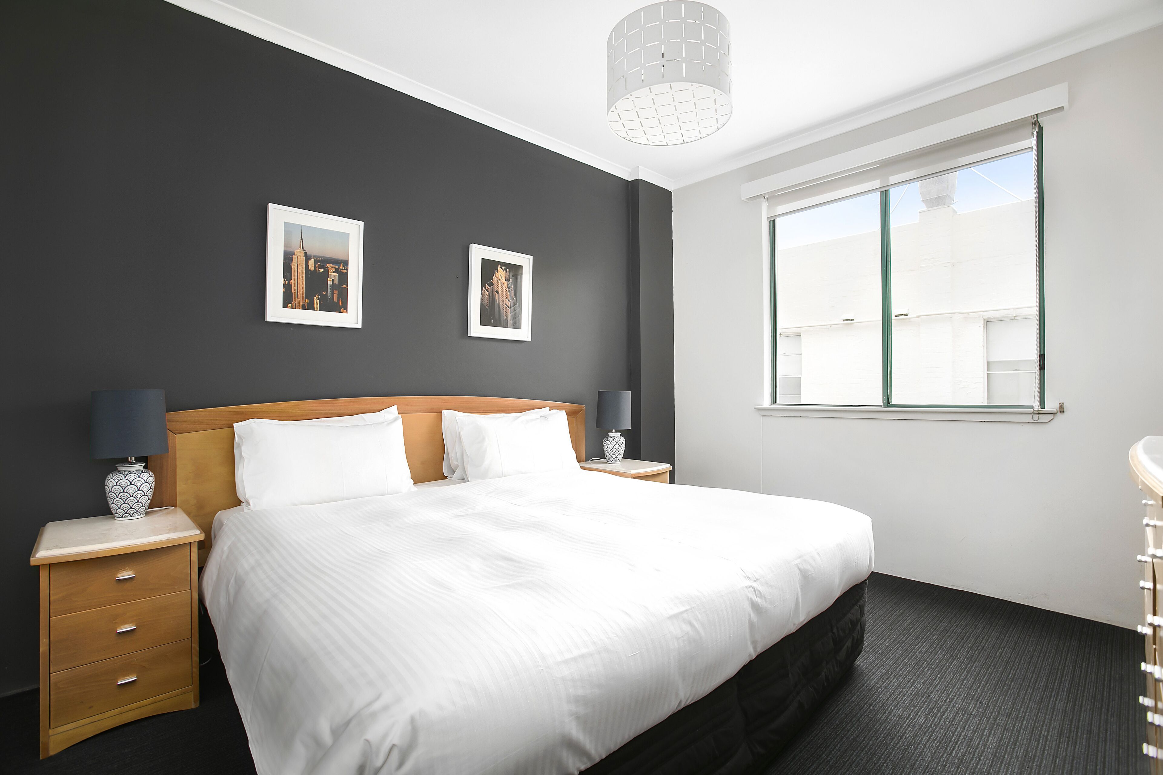 A hotel room with a large bed, two bedside tables with lamps, a window with a view, and two framed pictures on the wall.