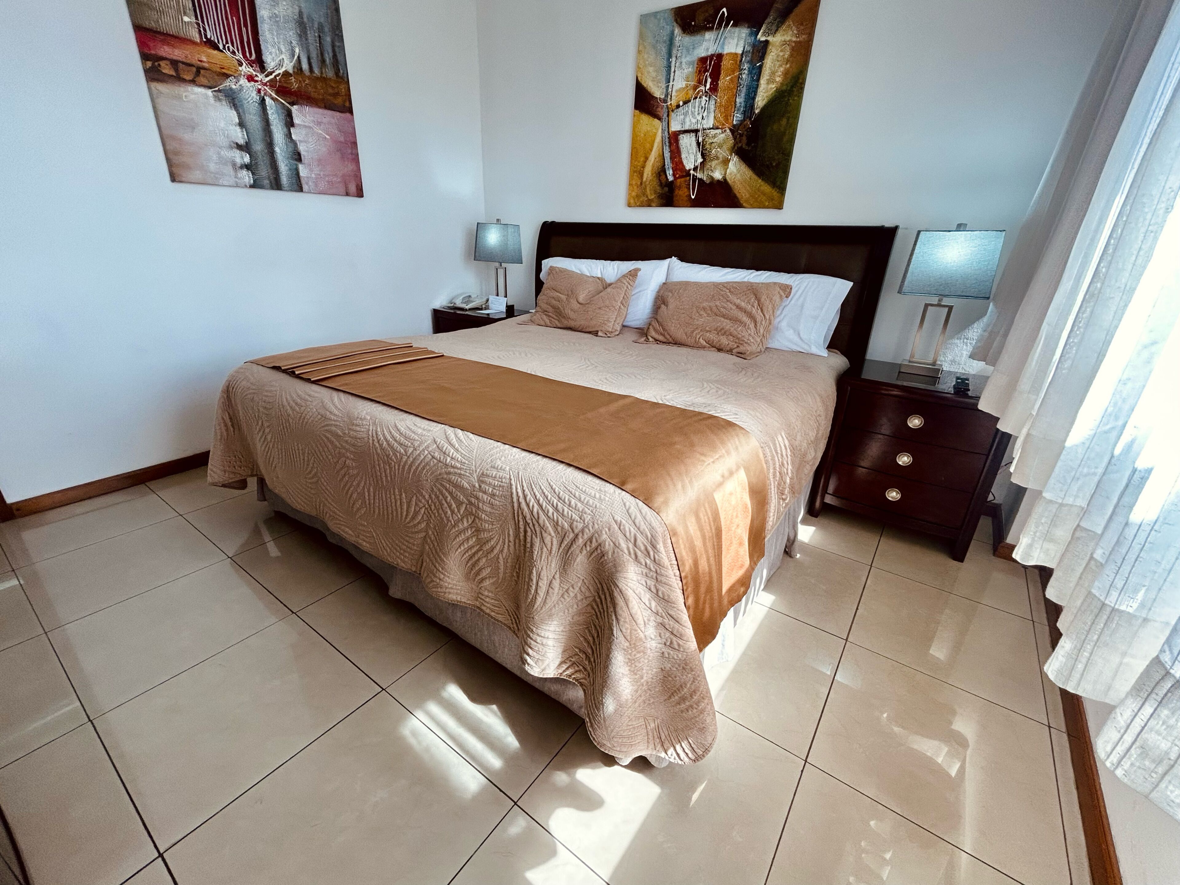 Una habitación de hotel con una cama grande, una mesita de noche con lámpara y obras de arte en las paredes.
