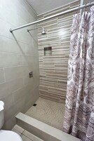 Zona de ducha con puerta de cristal, barra de apoyo metálica y cortina de ducha estampada.