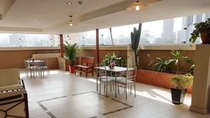 A spacious indoor area with a dining table and chairs, surrounded by potted plants and a large window offering a city view. - Hotel Las Palmas (Lima)