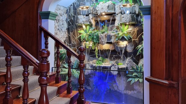 A wooden staircase leading to a room with a stone wall and a water feature. - Hotel Las Palmas (Lima)