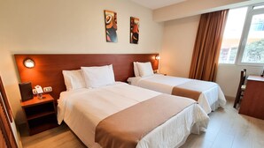 A hotel room with two beds, a nightstand, a desk, and a window with curtains. - Hotel Las Palmas (Lima)