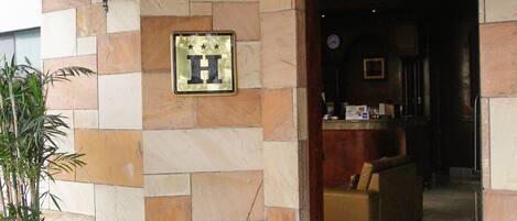 A hotel entrance with a stone facade, a sign reading "ENTRADA," and a reception desk inside.