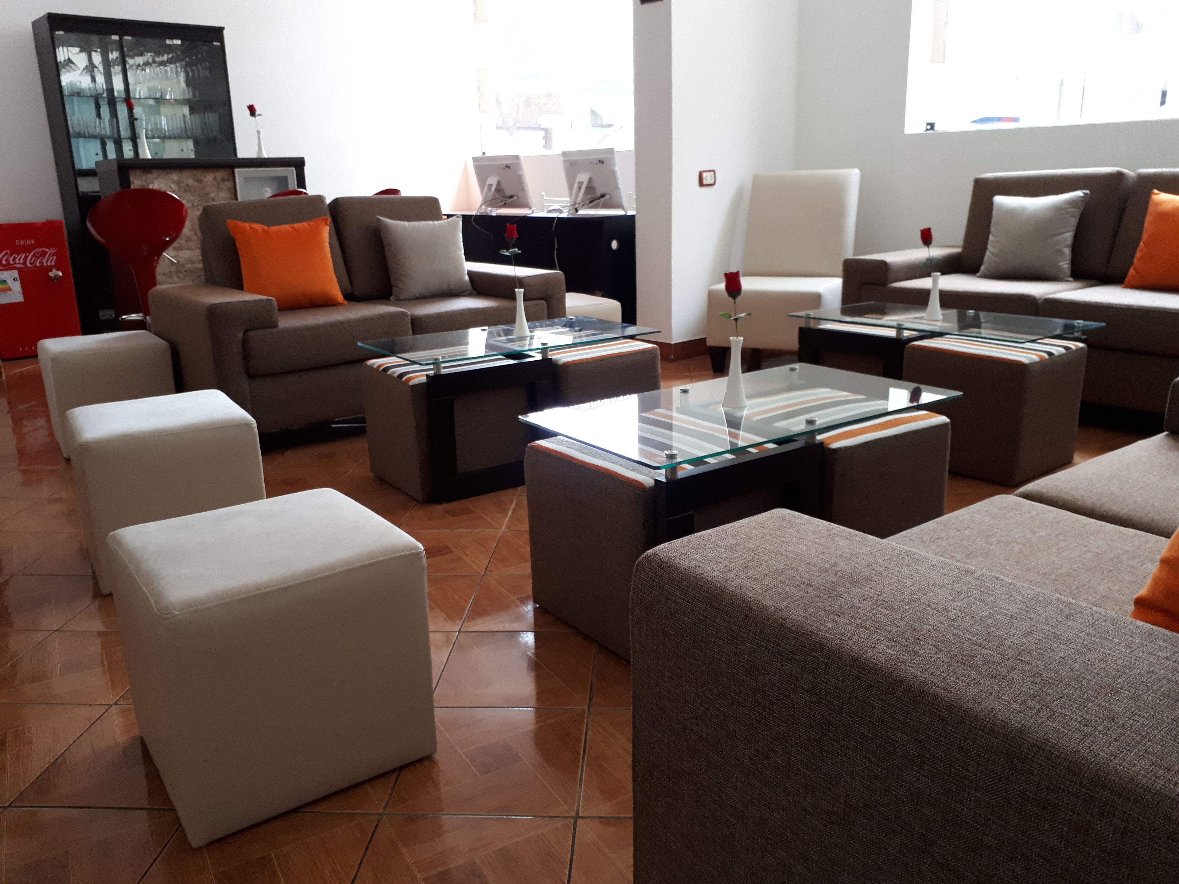 Ein modernes Wohnzimmer mit Sofas, Poufs und einem Glastisch. Auf einem Schreibtisch stehen zwei Computerbildschirme.