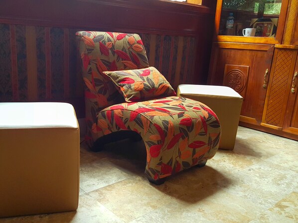 A chair with a floral pattern, a small table beside it, and a wooden cabinet in a room with patterned wallpaper.