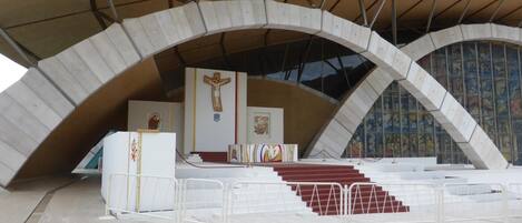 Una estructura arquitectónica moderna con una gran entrada en arco, un altar central con una cruz y una escalera que conduce al altar.