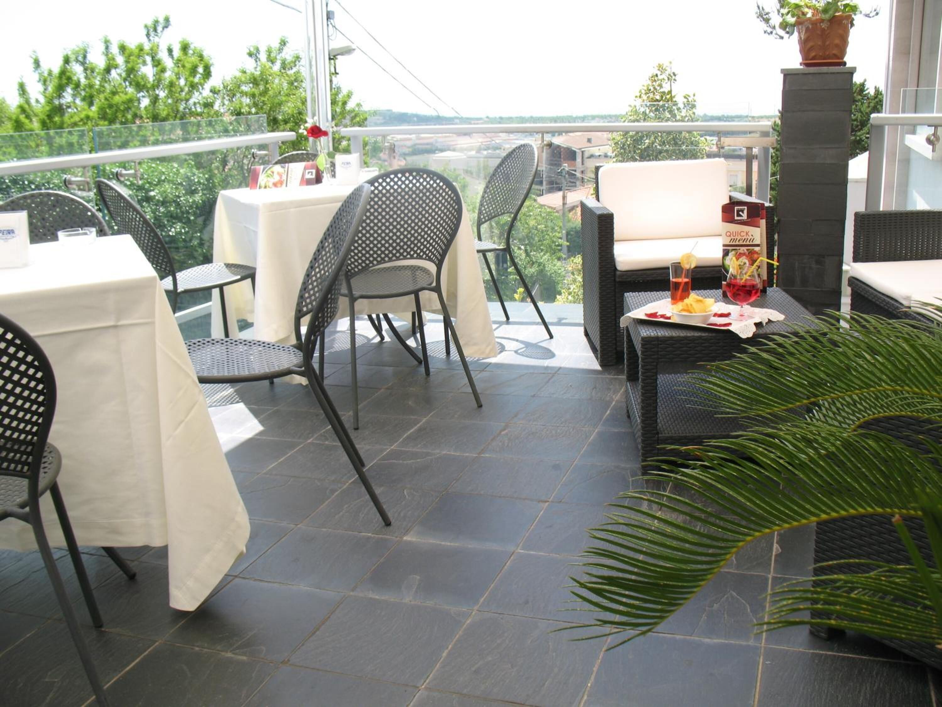 Una terraza con mesas al aire libre, una bebida sobre una mesa y una planta en maceta.