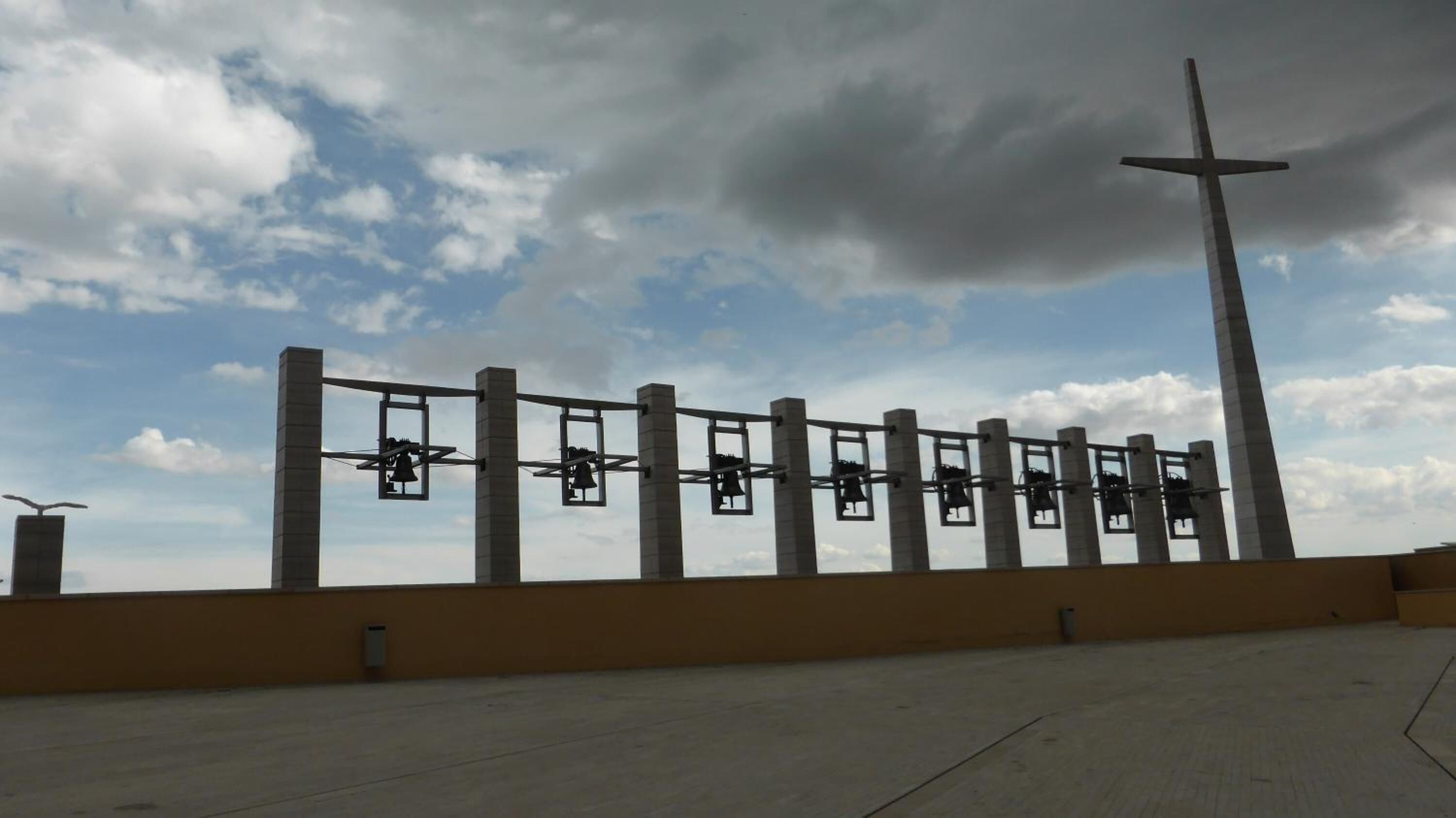 Un amplio espacio al aire libre con una estructura en forma de cruz y una serie de objetos con forma de campana.